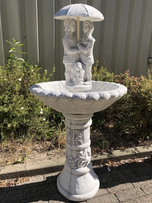 Gartenbrunnen voller Steine mit Kindern unter einem Regenschirm, sehr schön!